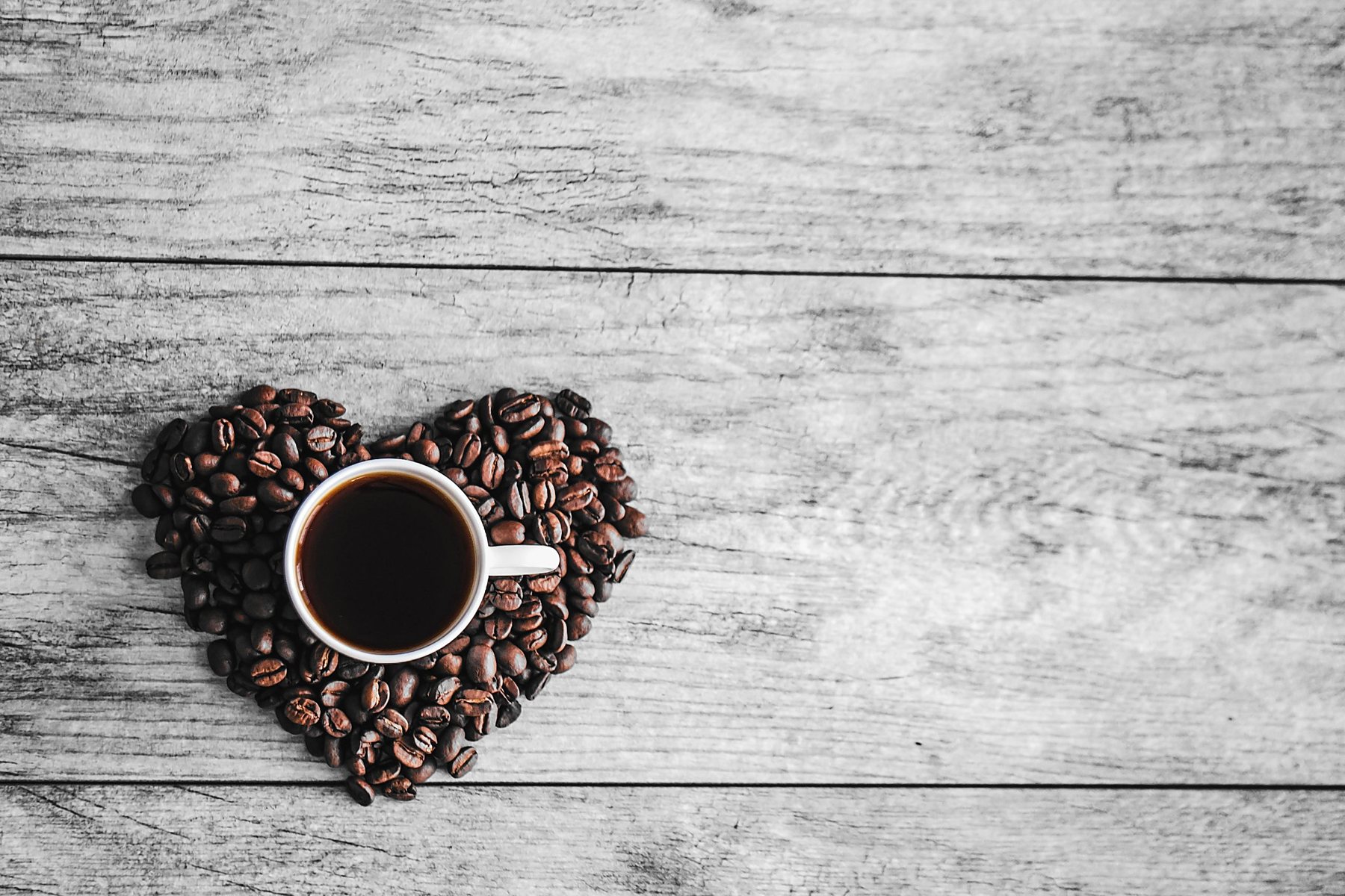 A cup of black coffee resting on a heart made of coffee beans