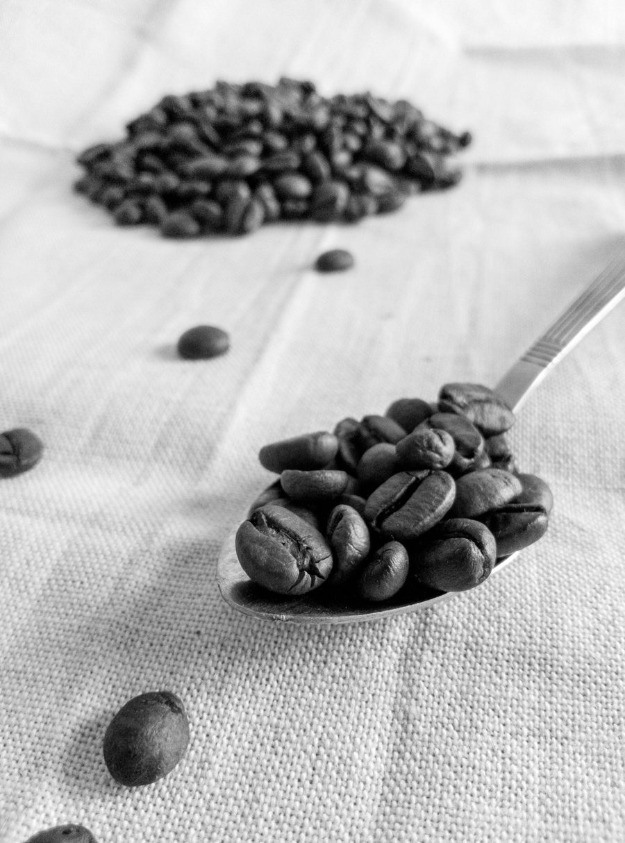 A spoonful of roasted coffee beans on linen, with more beans behind